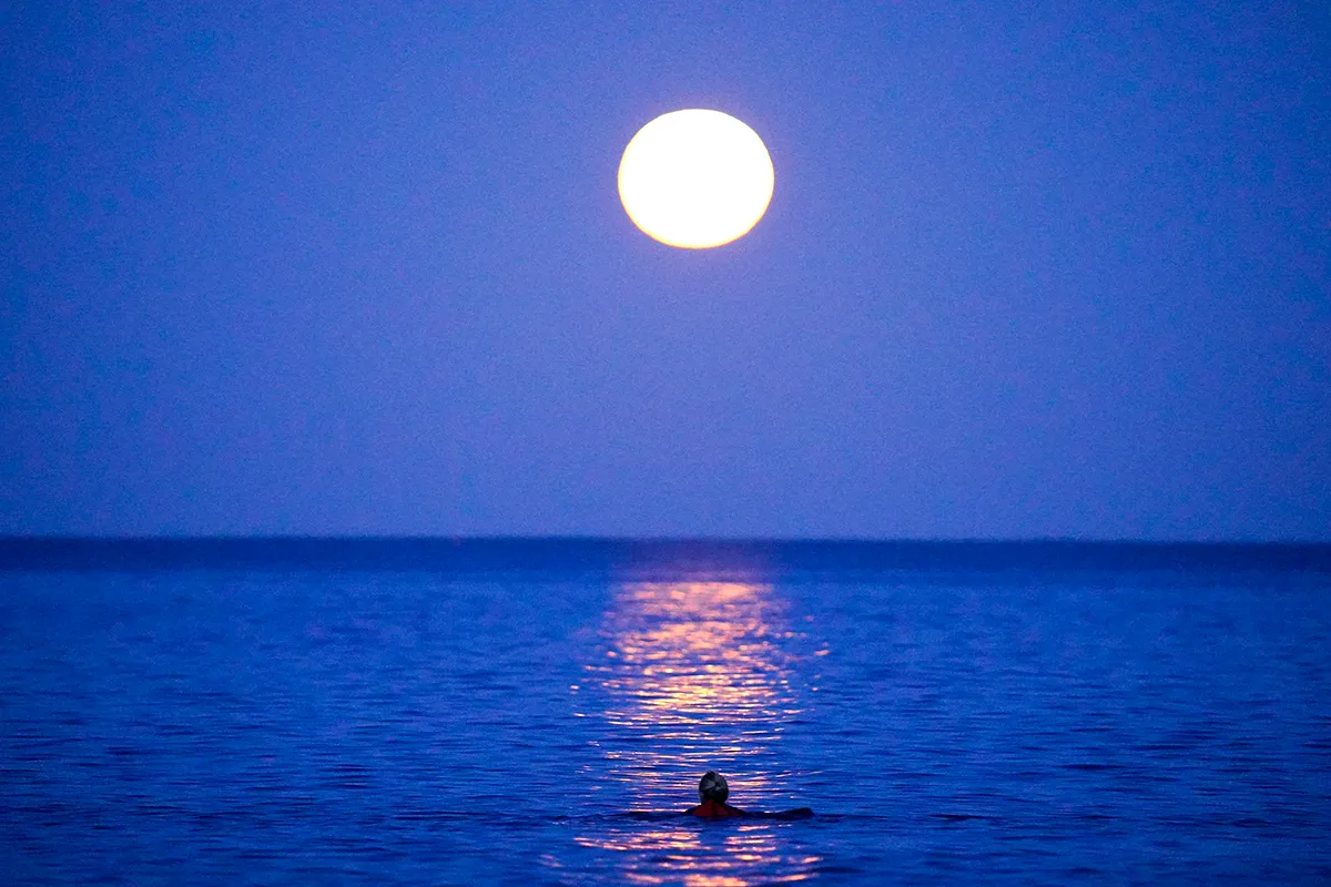 FALMOUTH, ENGLAND - SEPTEMBER 20: A lone swimmer takes to the sea to swim under the Harvest Moon on September 20, 2021 in Swanpool Beach, Falmouth, England. (Photo by Hugh R Hastings/Getty Images)
