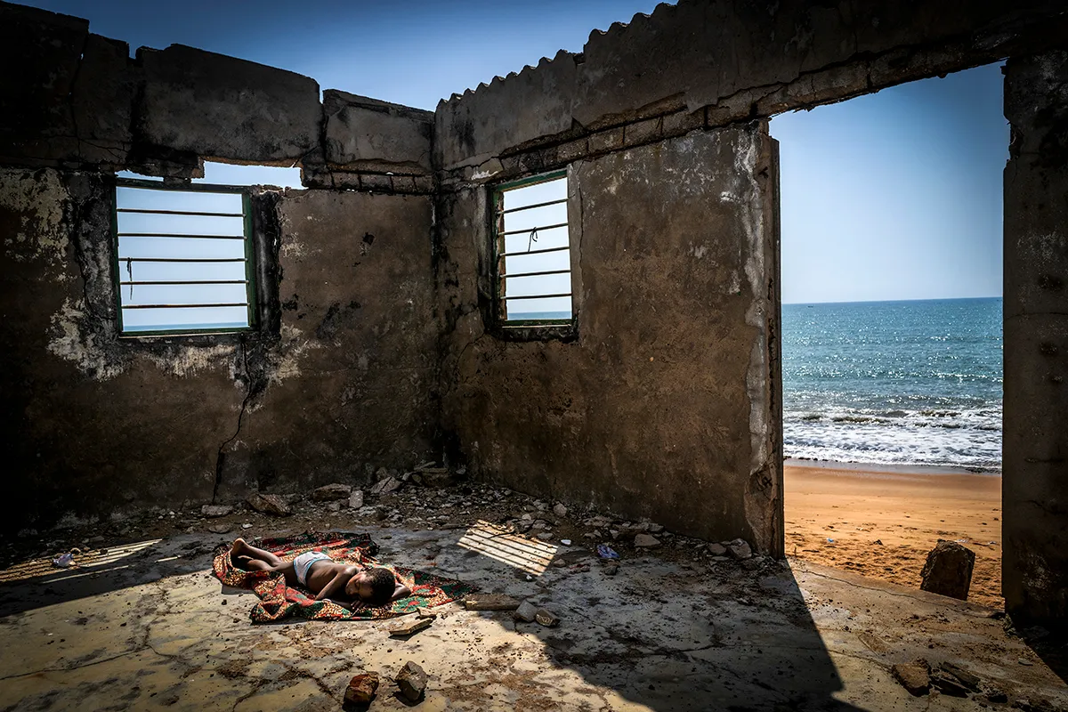 A child sleeps on the floor of his house about to collapse, destroyed by coastal erosion on Afidegnigba beach. Sea levels off the coast of Togo and other West African countries continue to rise and swallow up everything in their path. Homes, crops, roads, trees, schools, jobs, resources… lives. However, the shore of this small country in the Gulf of Guinea is only one part of the massive problem that affects more than 8,000 kilometers of seacoast in 13 West African countries. Punished by global warming, rising sea levels are forcing the ocean floor to readjust by removing sediment from the coast and washing it away from the shore. This causes marine erosion capable of devouring dozens of meters of land each year. As a result of this environmental global problem, thousands of people (mainly women and children) have already forced to leave their homes and migrate inland in search of food, shelter and to avoid a certain death… Many thousands more await their inexorable future... That next rising tide that takes everything away.