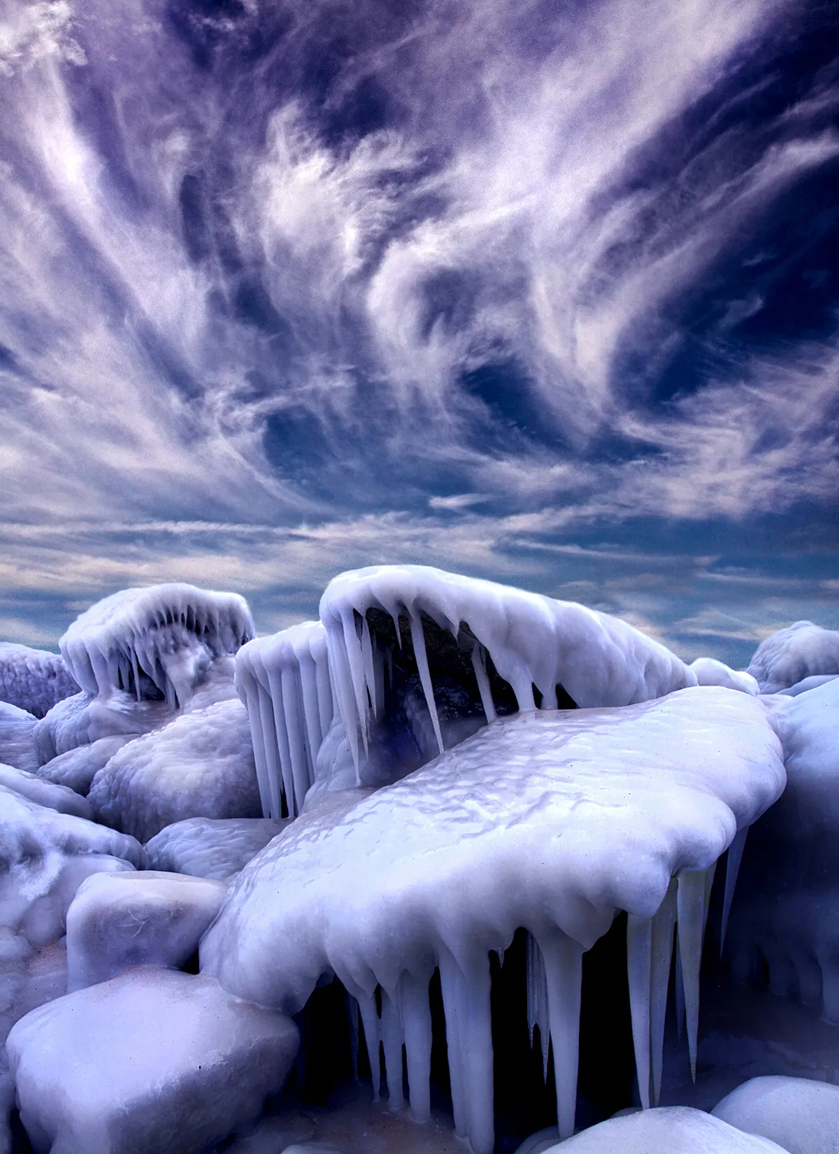Extreme cold and wind-blown spray combine to create a spectacular ice-bound landscape on the shores of Lake Michigan in Wisconsin, USA. For ice formations to build up like this, a substantial period of sub-zero temperatures is required in order for the surface of the lake to freeze. The time lag between the onset of sub-zero air temperatures and the freezing of the lake is due to the large heat capacity of water – a great deal of energy must be lost to the surroundings in order for the temperature of the lake to decrease appreciably, and so the lake cools much more slowly than the surrounding land surface and overlying air. Early in the winter, when the lake is still ice-free, but air temperatures are already well below freezing, waves crashing onto the shore create spray that freezes quickly on contact with objects near the shoreline. Photo by Phil Kock