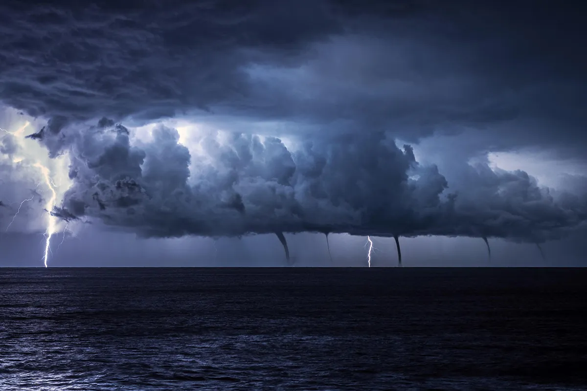 A rare spectacle unfolds as multiple waterspouts develop underneath the base of a line of storms over the Adriatic Sea, as seen from near Mali Losinj, Croatia. Waterspouts are simply tornadoes occurring over water. They are particularly common in the autumn and early winter months over the Mediterranean Sea and adjoining water bodies, when outbreaks of cold air spread over the still- warm waters, creating strong instability. In this example, the fact that the waterspouts are arranged in a line suggests that they have developed along a well-defined convergence zone – a boundary where winds of differing speeds and directions meet. As the air converges it is forced to rise, creating a line of towering clouds. The differing wind speeds and directions generate spin along the boundary which, when ingested by the rising air and stretched in the vertical, may be amplified to tornadic strengths, resulting in development of the waterspouts. Photo by Sandro Puncet