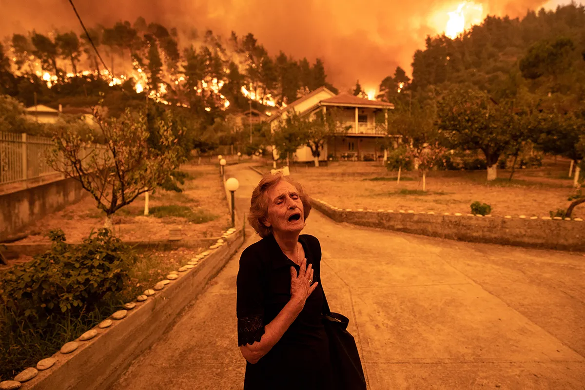 An elderly lady leaves her home threatened by wildfire in the village of Gouves, on the island of Evia, Greece, on Sunday, Aug. 8, 2021. Photographer: Konstantinos Tsakalidis/Bloomberg via Getty Images