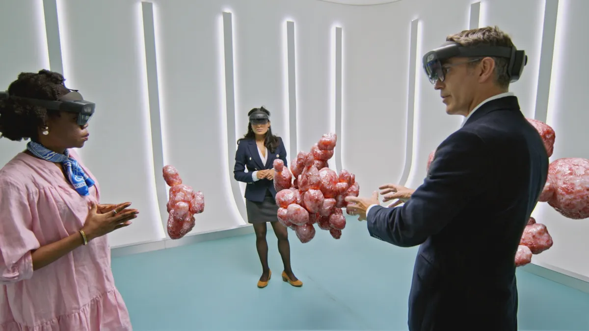 Three people wearing augmented reality headsets are standing around a 3D graphical representation of some fibroids in a uterus
