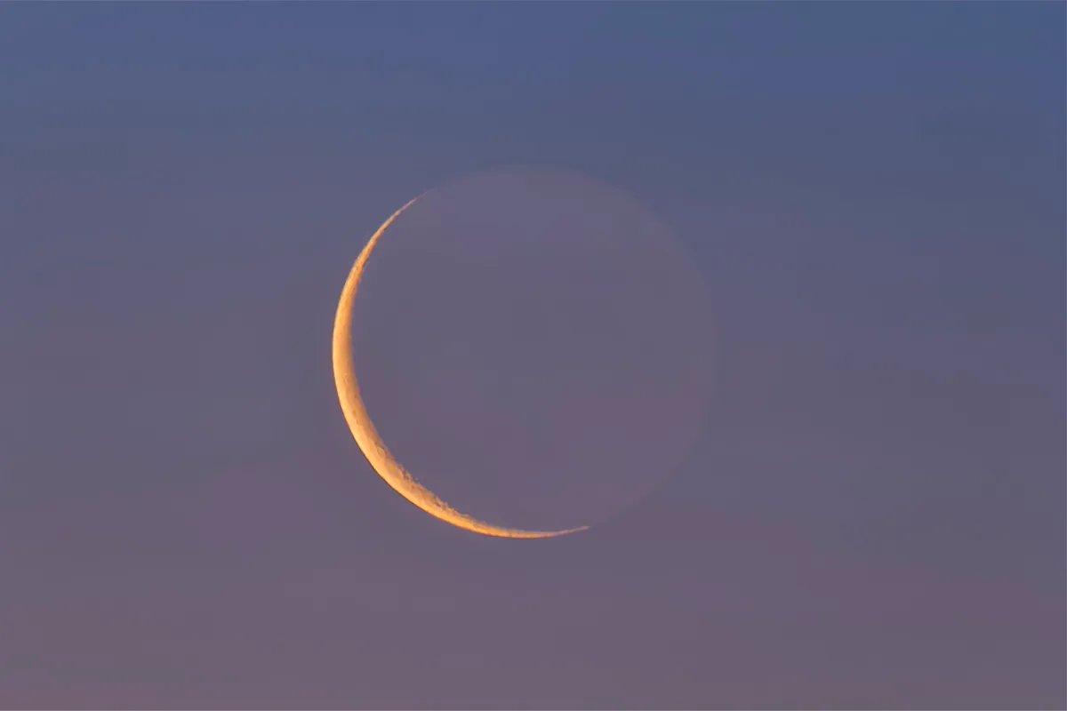 The thin waning 26-day-old Moon low in the dawn sky and reddened from the low altitude and twilight colours, but still showing some Earthshine on the dark side of the Moon. Image credit: Getty images