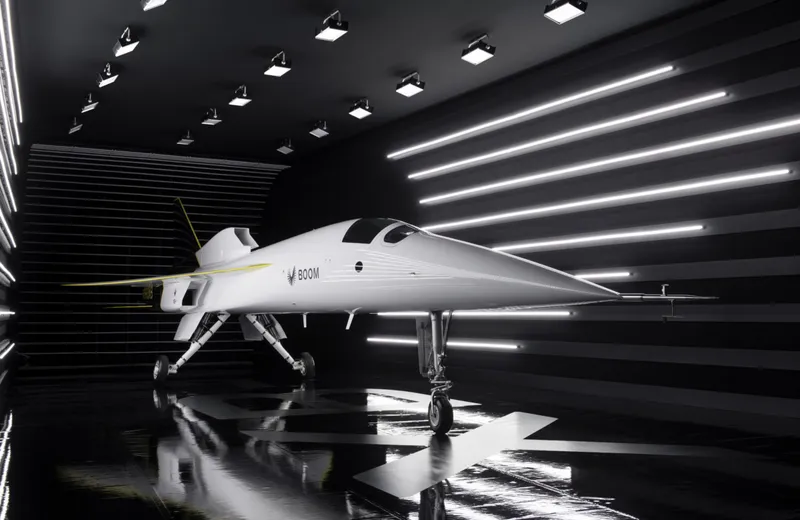 The front of a white XB-1 supersonic aircraft in a dark room with bright lights