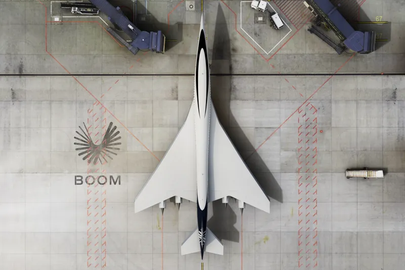 Aerial view of a sleek white supersonic aircraft with the words BOOM printed on the grey floor