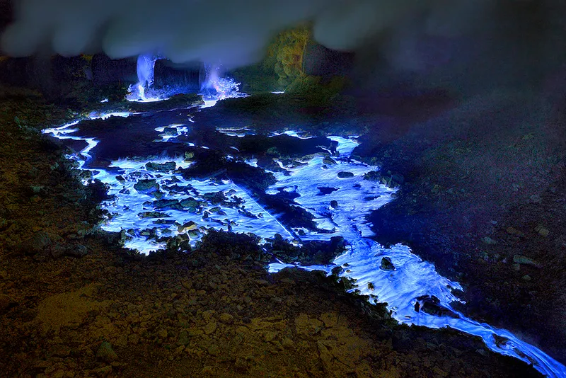 A river of neon blue lava appears luminous as it flows over volcanic rock