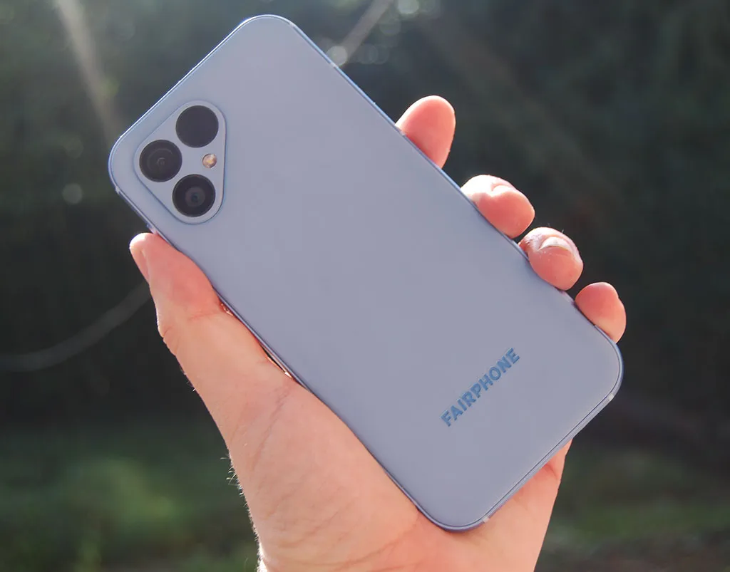Hand holding the Fairphone 5, showing the blue back of the smartphone.