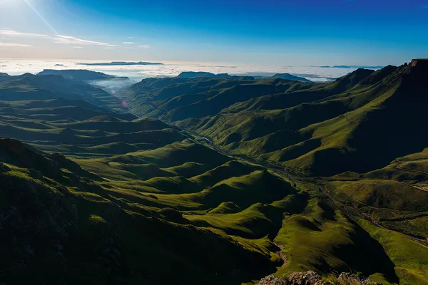 The view from Sani Pass to the Drakensberg mountain range in Africa, and shows big, green, undulating relief towards blue skies