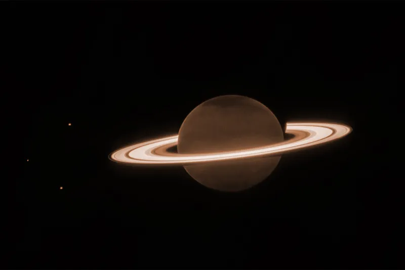 Planet Saturn in brown with white ice rings and three small Moons in orbit, pictured by the James Webb Space Telescope. 