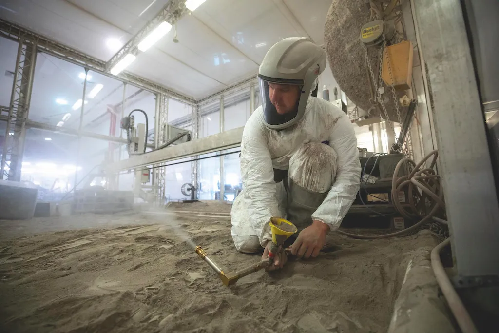 A photograph of a NASA researcher wearing protective clothing, creating a fine spray of moondust simulant