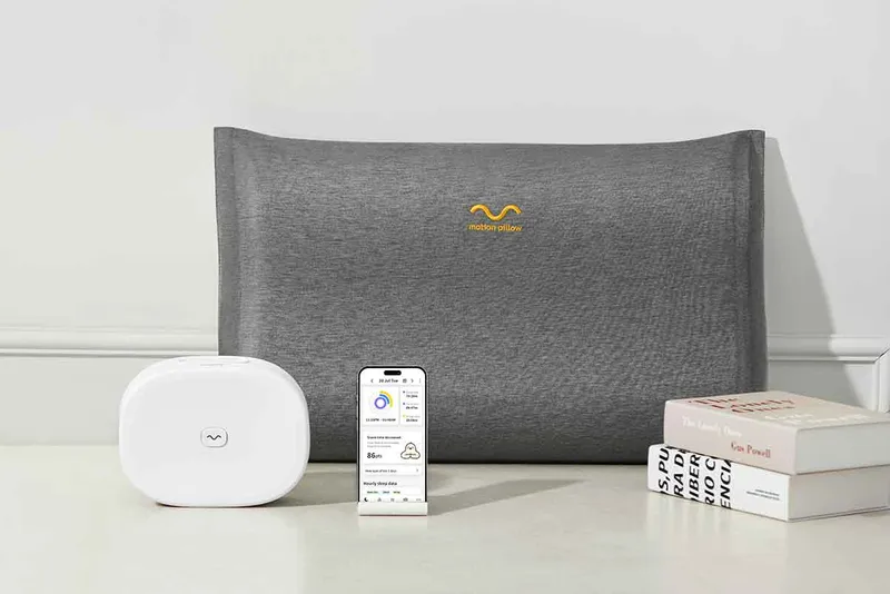 The Motion Pillow, as well as remotes and its packaging sit against a white wall