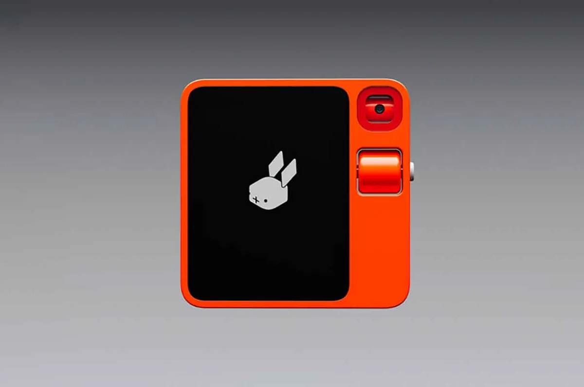 The Rabbit R1, a small orange handheld device, sits on a grey background