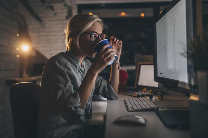 Woman drinking coffee by a desk at night