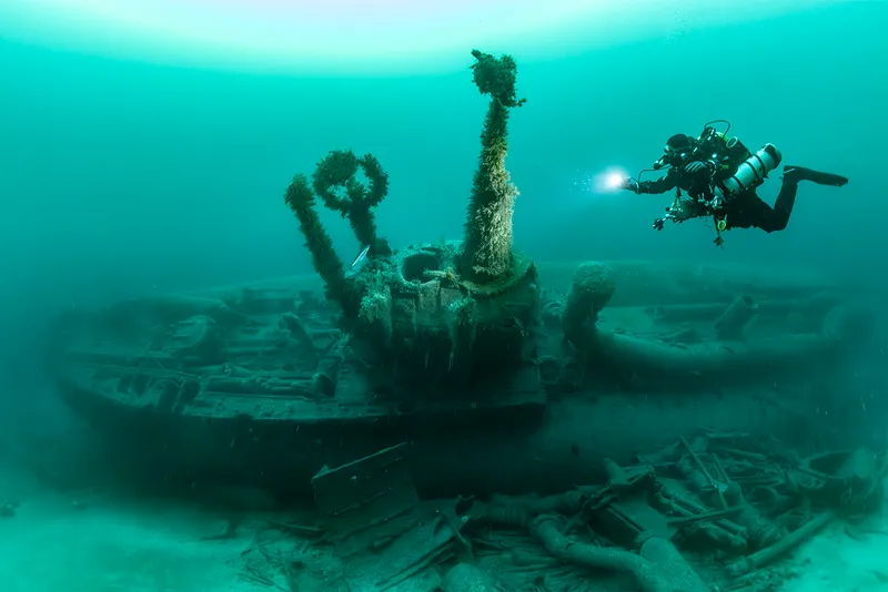 diver with torch above a ship wreck