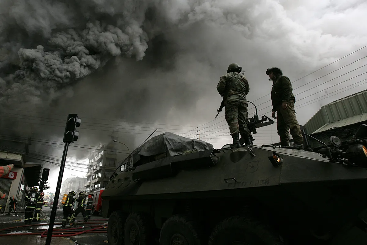 Soldiers stand on tank with black smoke in distance