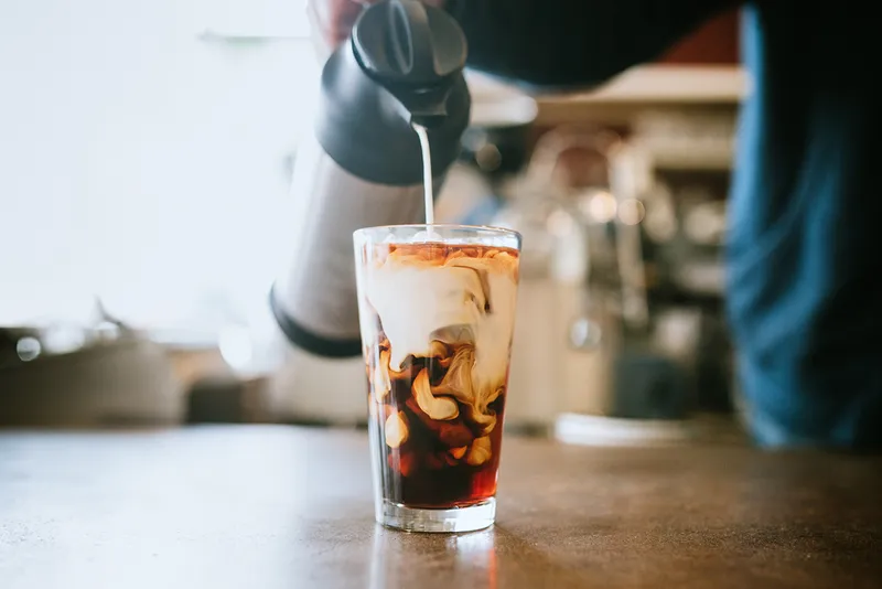 A man pours milk into a glass of cold brew coffee