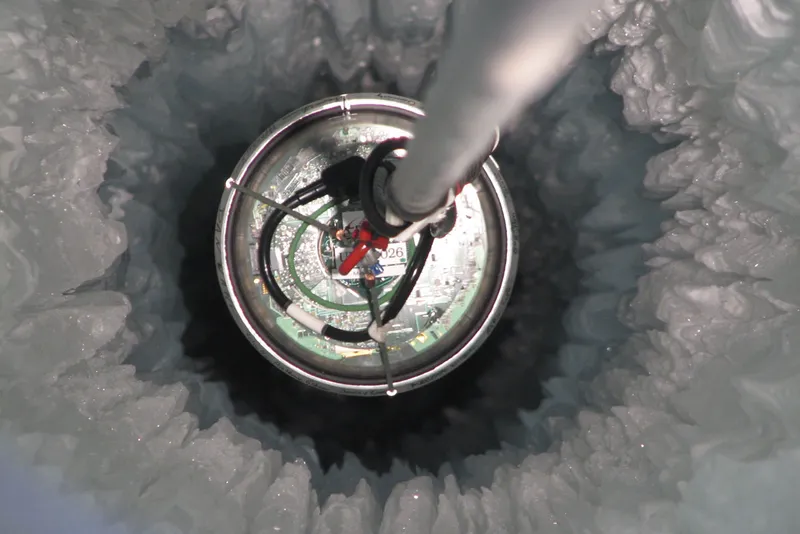 A circular metal device is lowered into a hole in the ice.