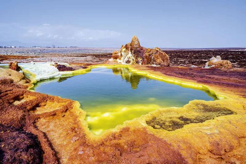 A bright blue body of water surrounded by strange yellow, orange and red rock.