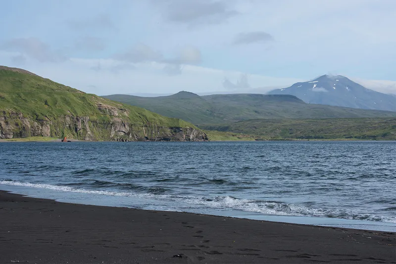 Bay with waves black sand and hills in distance