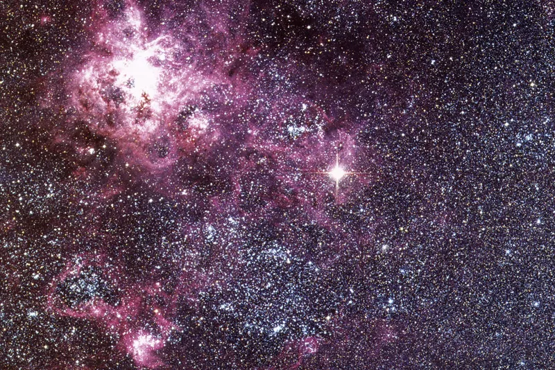 A colourful patch of the night sky filled with pink clouds and many white and blue spots of stars.