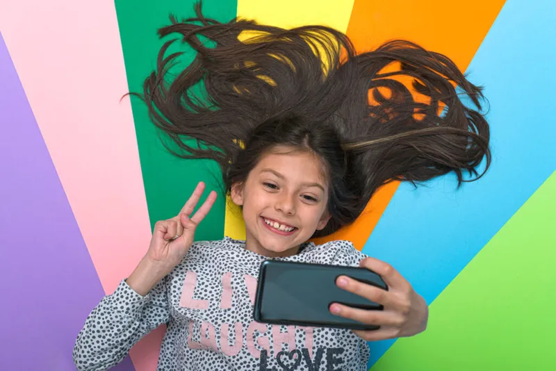 Little girl take a selfie lying on multicolour Background