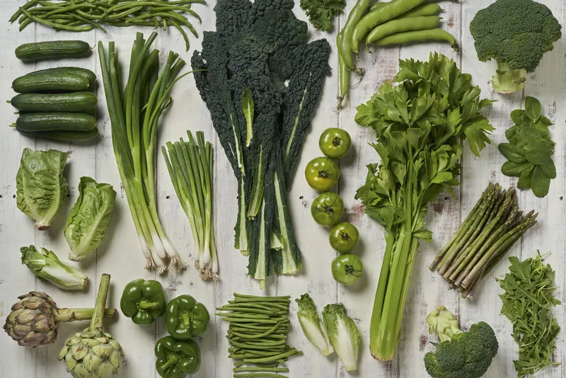 A selection of green vegetables arranged on a rustic white wooden table.