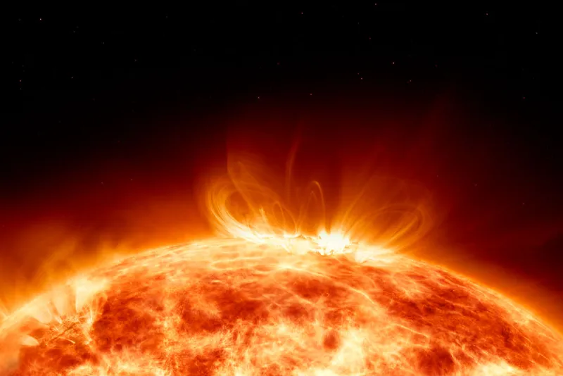The top of the Sun stretches across the bottom of the image. Flares of particles are spewing out from its edge.