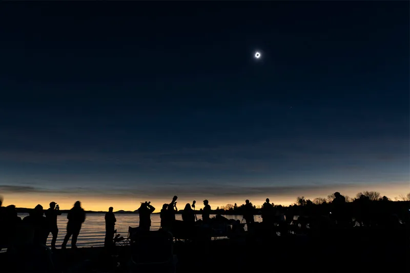 people on beach look up at total solar eclipse.