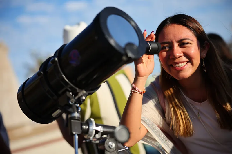 Smiling woman looking through telescope.