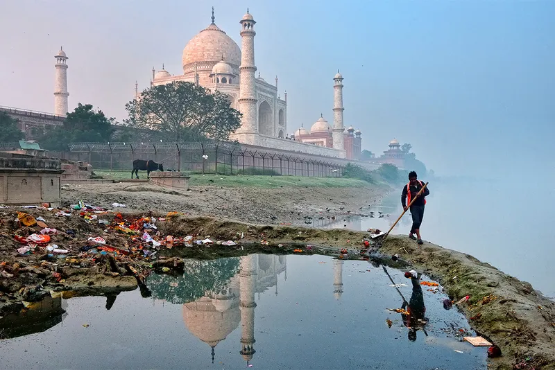 Man cleaning trash from water by Taj Mahal india