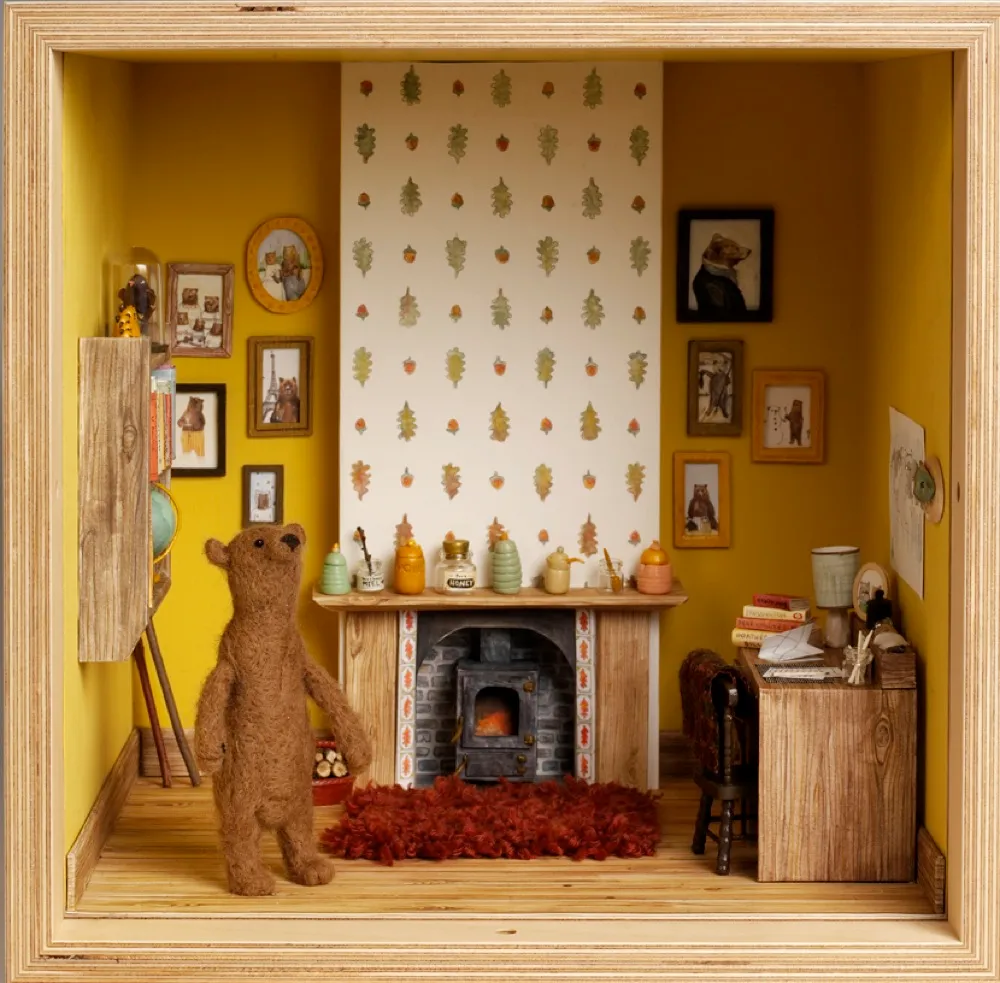 A dolls house living room with bold yellow walls adorned with paintings, a wood burning stove and a bear