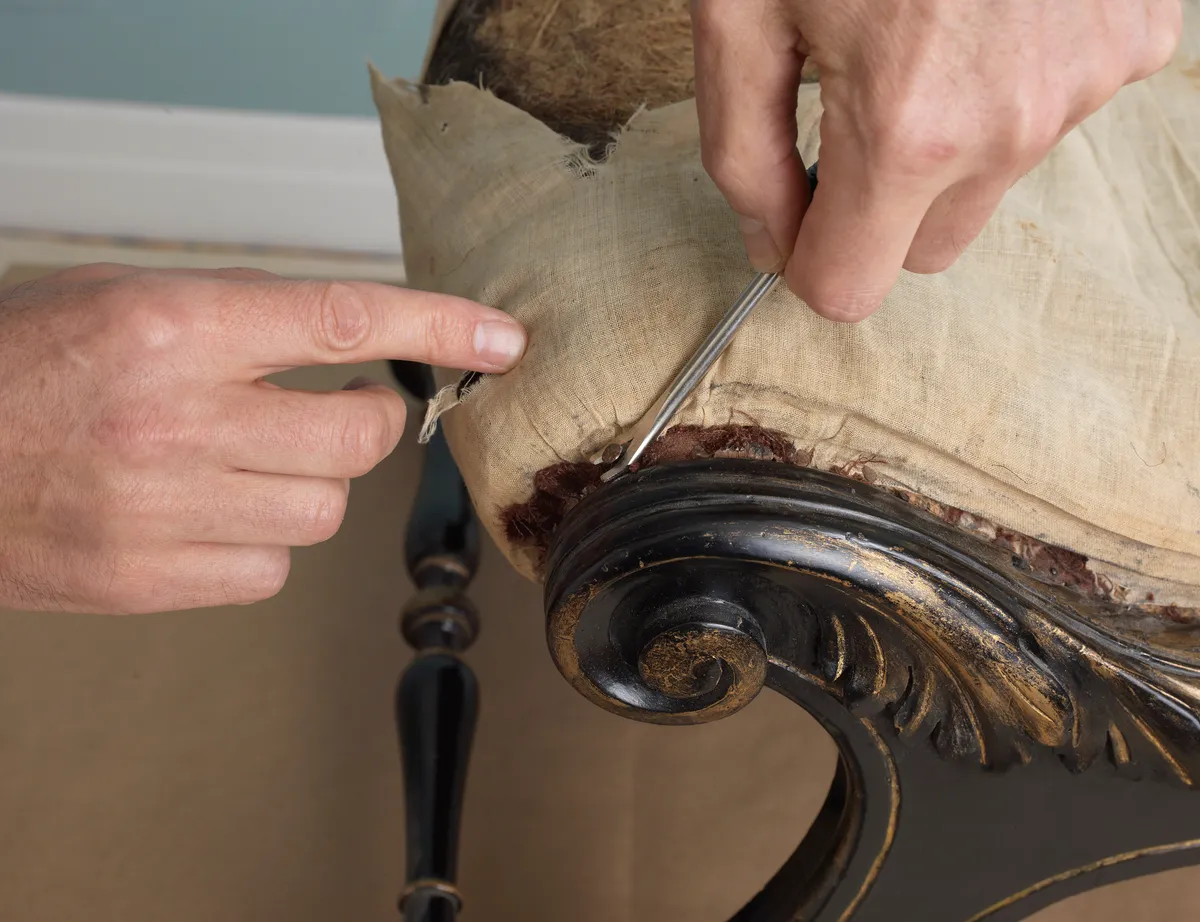 Someone peels back the upholstery on an antique dining chair