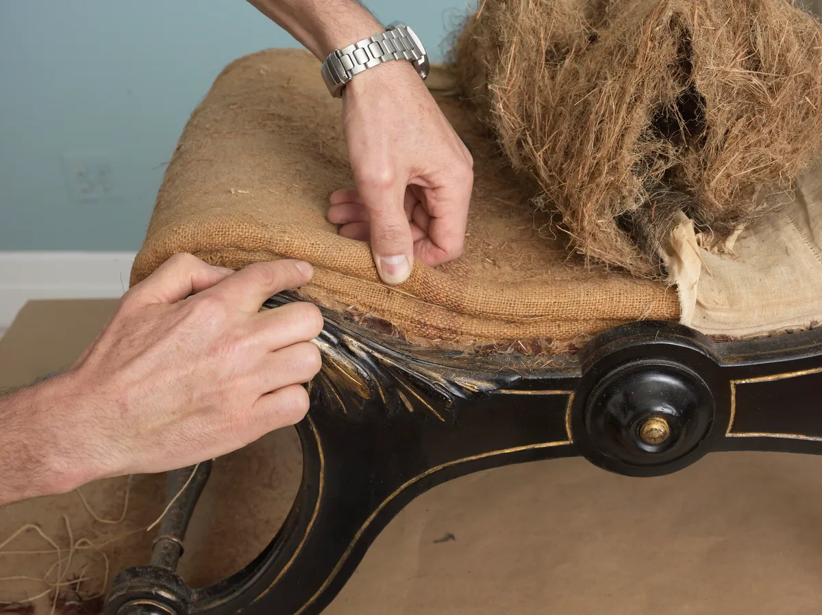 Someone peels back the upholstery on an antique dining chair