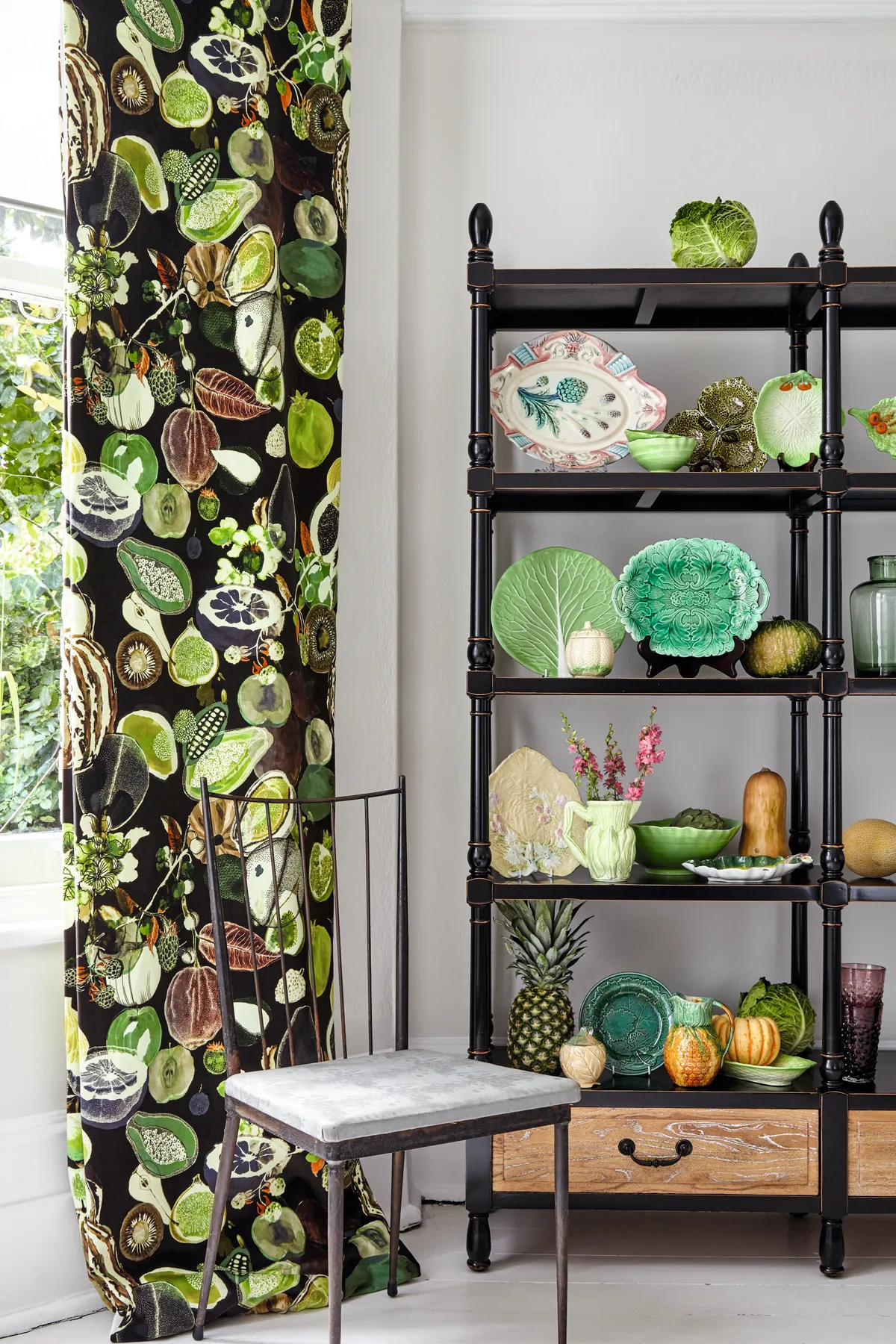 An array of fruit and vegetable plates on open shelving, with vegetable-print curtains to match