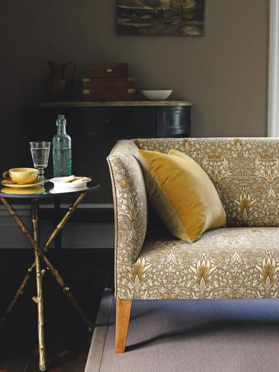 An Art Deco style sofa upholstered in yellow William Morris fabric against a dark living room wall