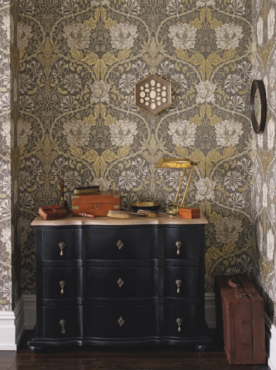 An antique sideboard painted black sits in front of patterned William Morris wallpaper