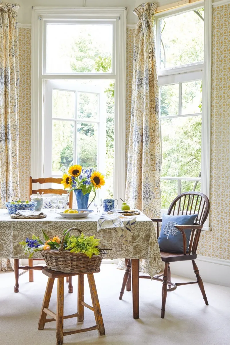 A summer dining scene: a table is covered with a William Morris table cloth and William Morris curtains hang behind