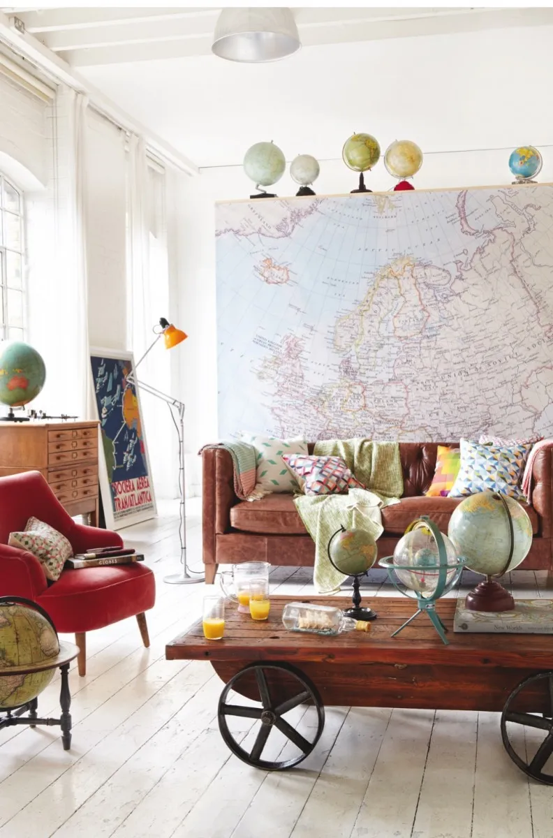 A living room with a brown leather sofa, red armchair and a coffee table littered with antique globes. A large antique map hangs on the wall behind the sofa.