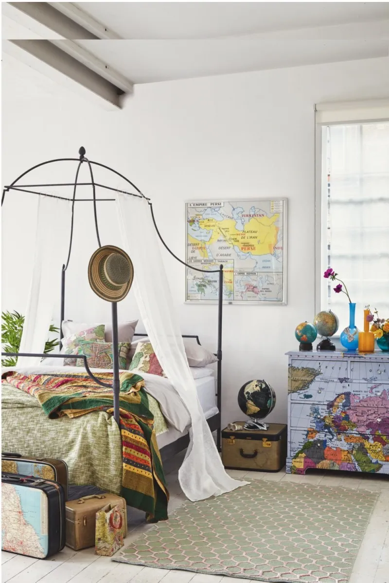 A bedroom with a black metal canopy bed and a chest of drawers painted to look like an antique map
