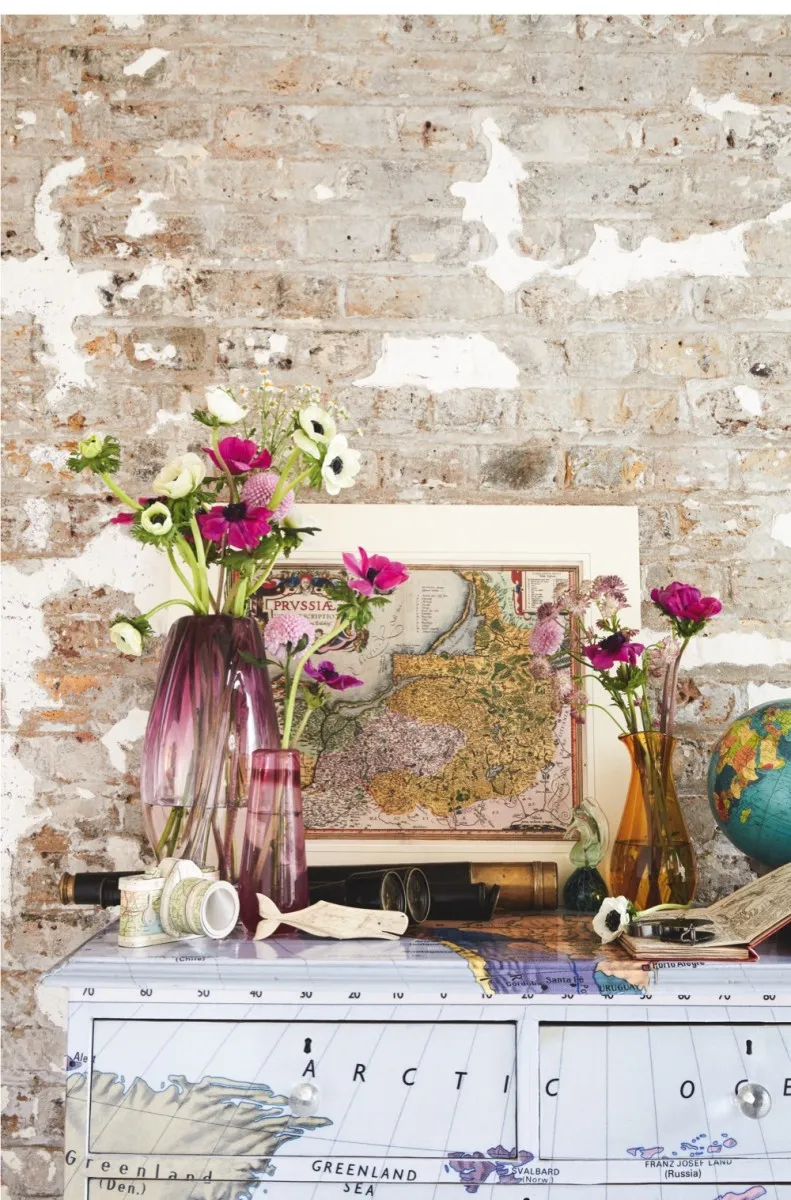A dressing table adorned with pink glass vases of flowers and a framed antique map
