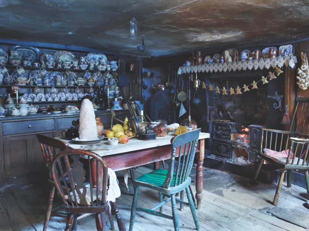 A low-ceilinged basement kitchen in Dennis Severs House with an open fireplace, a welsh dresser laden with china and a kitchen table laden with Christmas food