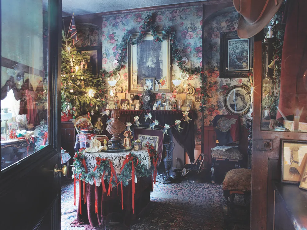 The Victorian parlour in Dennis Severs' House featuring a large real Christmas trees, ribbon garland and bold floral wallpaper
