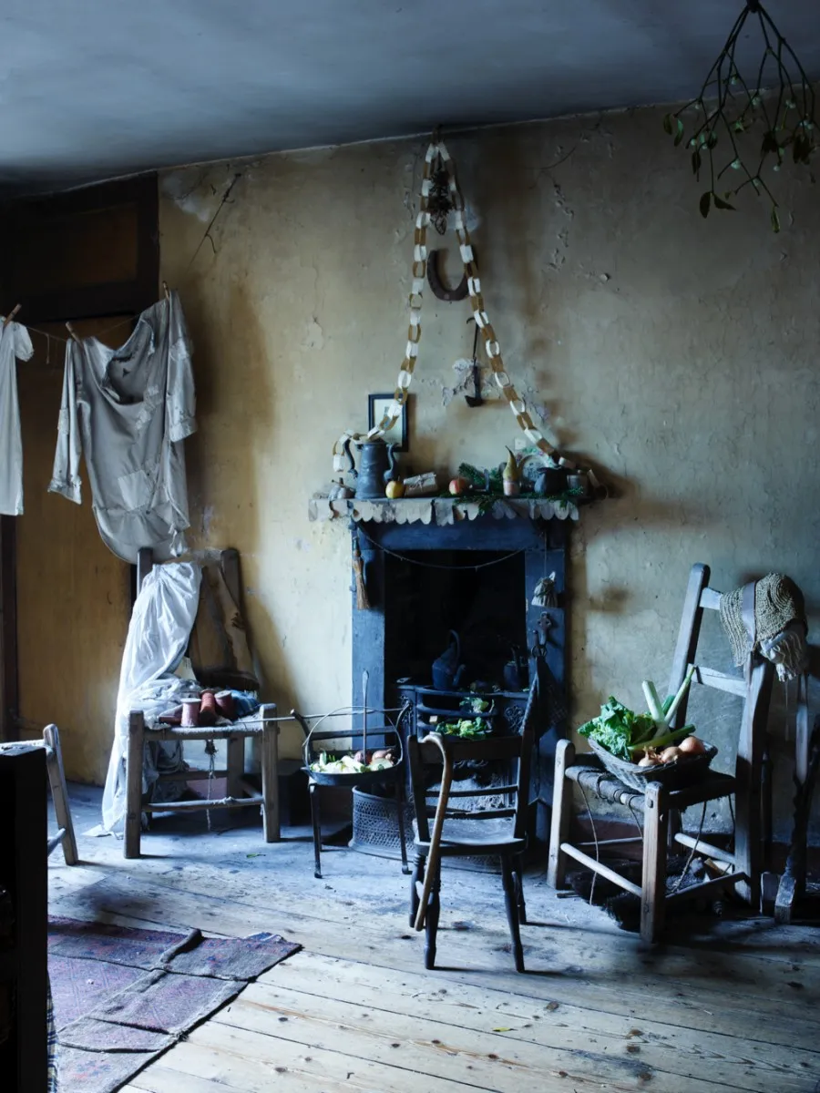 The attic bedroom in Dennis Severs' House. Simple wooden chairs surround a blackened fireplace and laundry hangs to dry