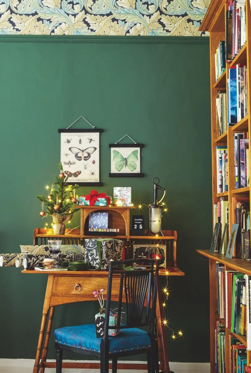 An office is decorated using William Morris wallpaper against a festive green wall. Vintage wall charts are hung above a liberty desk.