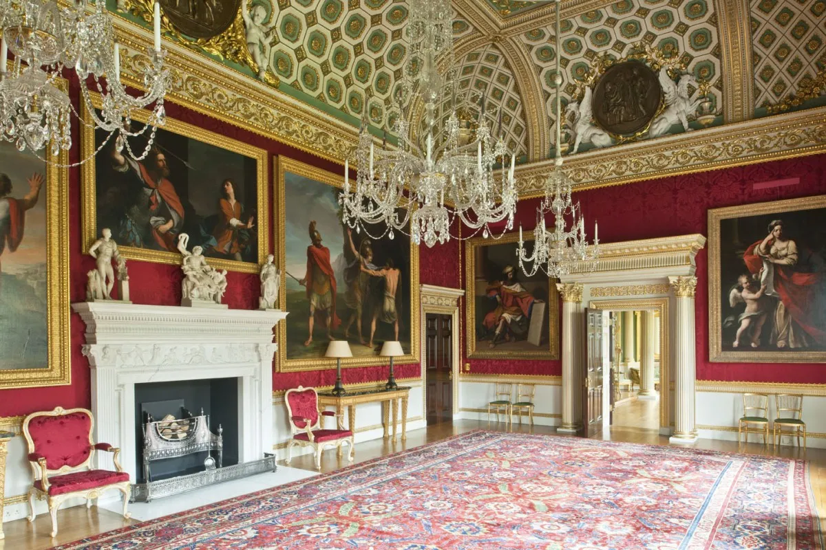 An entrance room in Spencer House. The walls are painted in rich red, and are adorned with large paintings of the hunt.
