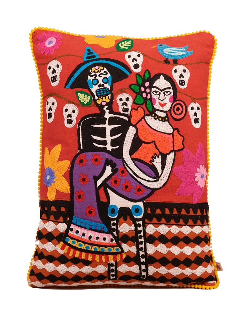 Vibrant and colourful Day of the Dead cushion. A skeleton man holds Frida Kahlo in his arms.
