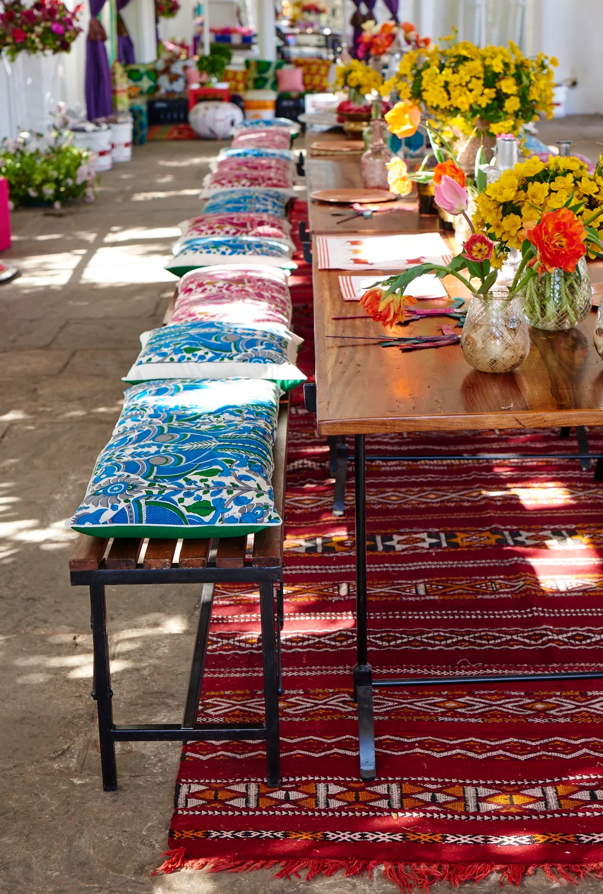 A long wooden and metal table with benched covered in colourful Indian cushions