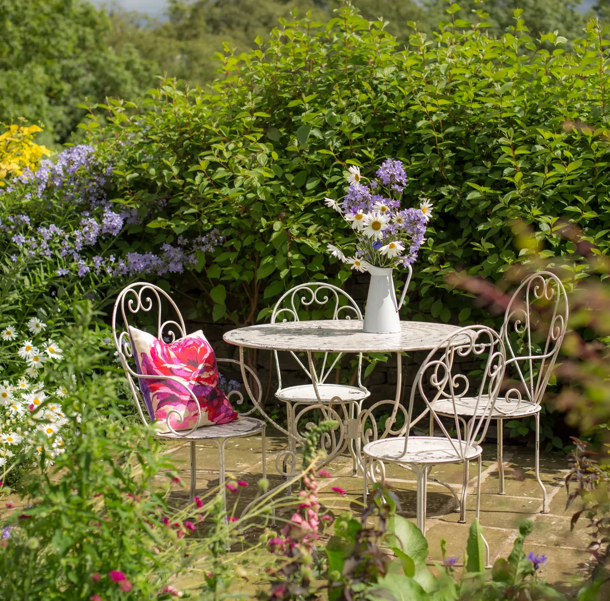 Elegant white metal patio furniture with an enamel vase of wild flowers