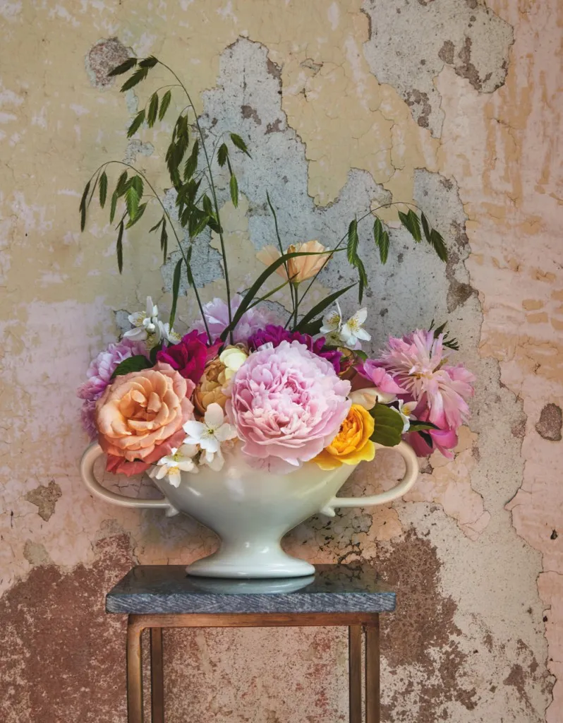 Constance spry vases filled with short peonies in front of an exposed plaster wall
