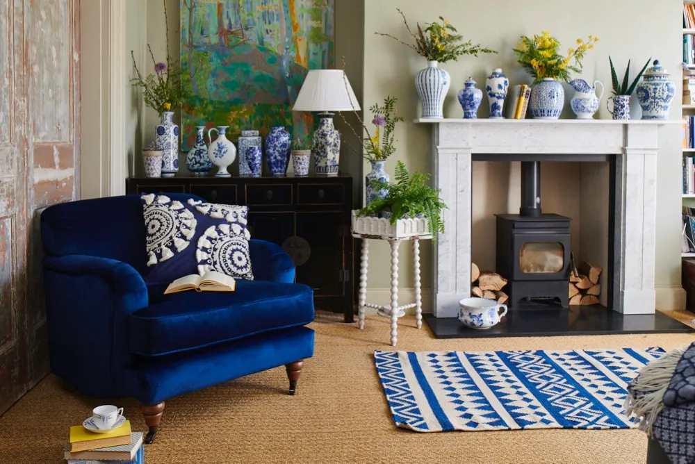 Stunning white and blue ceramics displayed on a mantelpiece beside a blue velvet armchair